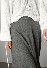 Maglione bianco lavorato a maglia con una vestibilità ampia e maniche larghe, abbinato a una gonna grigia fluida. La gonna presenta un aspetto morbido e testurizzato.