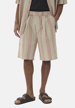 Pantalones cortos a rayas en beige, rojo y marrón, con una cintura elástica y tablones; combinados con sandalias marrones.