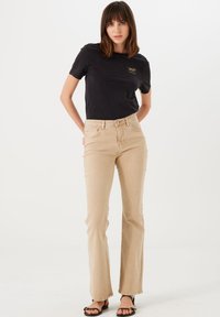 Camiseta negra de manga corta con un sutil gráfico de animal, combinada con jeans de campana beige claro. Modelo lleva sandalias negras con tiras.