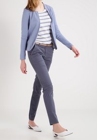 Ljusblå blazer över en vit och marinblå randig skjorta, i kombination med grå slim-fit byxor och vita spetsiga ballerinaskor. Enkel och modern design.