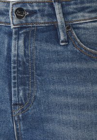 Jeans i denim i medelblå tvätt med en lätt blekning, med gyllene sömmar, klassisk femfickorsdesign och metallknäppning.