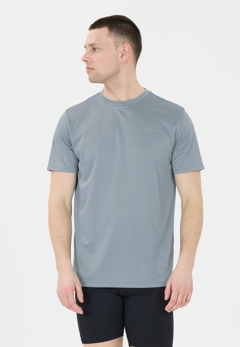 Harmaa lyhythihainen urheilupaita, joka on valmistettu sileästä kankaasta ja jossa on pyöreä kaula-aukko. Paidassa on hienovarainen logo vasemmalla rinnalla.