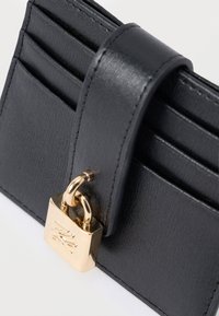 Portofel din piele neagră cu patru sloturi, o curea din piele și un accent cu un lacăt auriu. Textură netedă cu detalii subtile în granulație.
