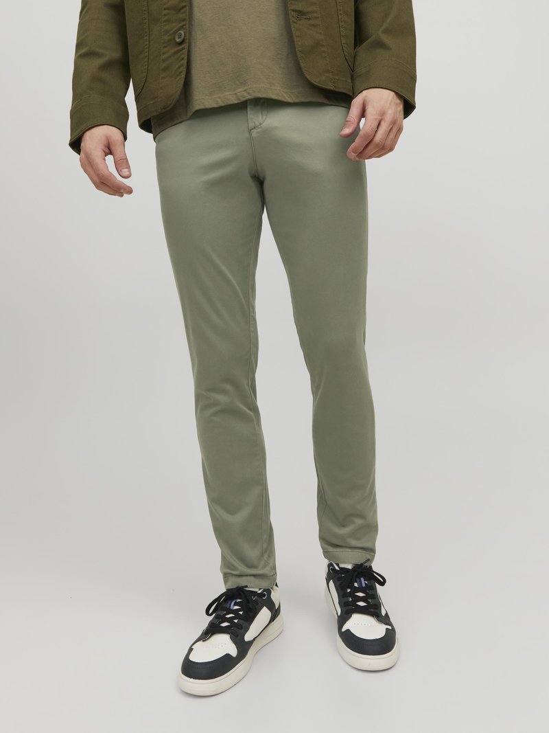 Zielone spodnie z bawełny w składzie, o slim fit, z gładką fakturą, kieszeniami z przodu, w połączeniu z czarno-białymi sneakersami.