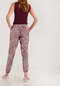 Bordowa koszulka bez rękawów, wzorzyste różowo-szare spodnie w panterkę, elastyczny pas, zwężane nogawki oraz jasnoróżowe buty wsuwane.