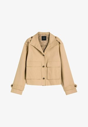 Beżowa krótka kurtka z dużymi kieszeniami z przodu, zapięciem na guziki, szerokim kołnierzem oraz regulowanymi mankietami na guziki, prezentowana na białym tle.