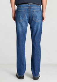 Jeans blu in denim con design a gamba dritta, dotati di due tasche posteriori e una finitura testurizzata. La cintura è scura con un'etichetta in pelle.