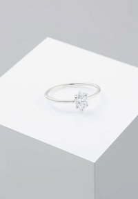 Anello in argento con una pietra trasparente a taglio marquise, montato su una sottile fascia. Esibito su un pedistallo bianco minimalista.