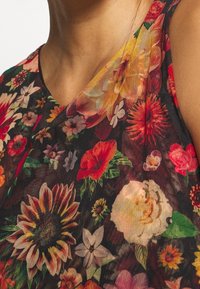 Haut sans manches floral en tissu en mesh noir orné de fleurs vibrantes en rouge, jaune et blanc, avec une texture douce.