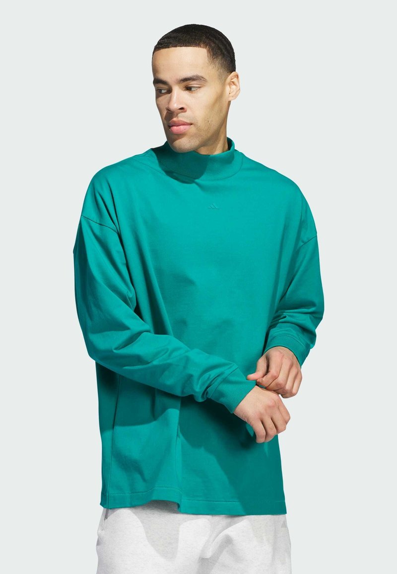 Chemise turquoise à manches longues avec un col montant, coupe ample et poignets côtelés. Fabriquée en tissu doux avec un minimum de branding sur la poitrine.
