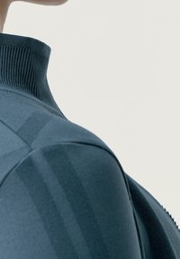 Maglietta sportiva blu scuro con colletto alto, tessuto a maglia texturizzato e motivo a righe sottili lungo la spalla e il lato.