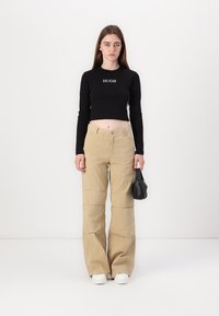 Crop top nero a maniche lunghe con logo "HUGO", abbinato a pantaloni cargo beige a gamba larga con dettagli cuciti, tenuto con una borsa nera.