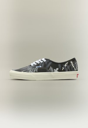 Zapatilla Vans en blanco y negro con estampado floral, cordones blancos y suela blanca gruesa sobre fondo neutro.