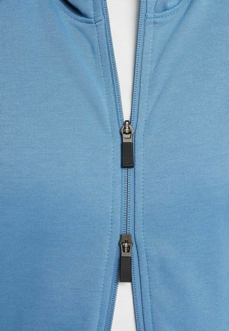 Nahaufnahme eines blauen Stoffreißverschlusses mit zwei schwarzen Metallzippern, teilweise über einem weißen Hintergrund zippt.