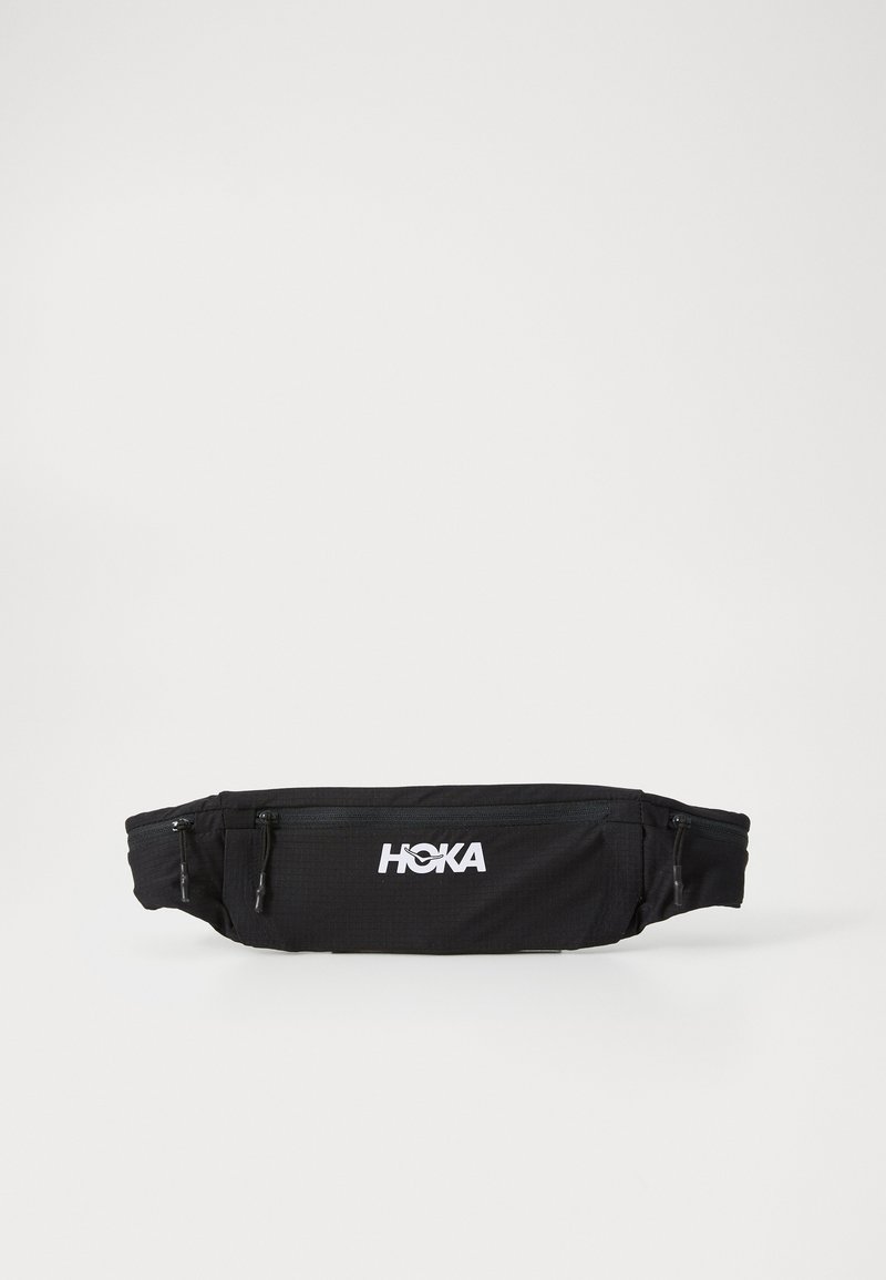 Mustahdutus musta vyö kott made of lightweight fabric, jossa on kaksi vetoketjullista osastoa ja muhkea valkoinen "HOKA"-logo edessä.