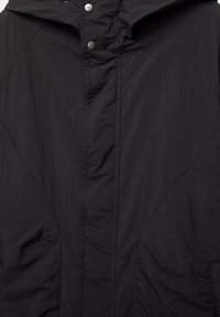 Giacca nera realizzata in tessuto leggero e resistente all'acqua. Presenta una chiusura frontale a scatto, cappuccio e tasche laterali. Texture liscia con poche pieghe.
