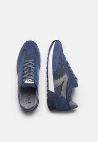 Scarpe di camoscio blu con accenti in tessuto, lacci grigi e suola in gomma bianca. Presentano cuciture gialle e un design sportivo.