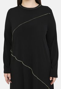 Schwarzes Langarmkleid mit einer geschwungenen goldenen Akzentlinie an der Vorderseite. Der Stoff wirkt glatt und hat einen lässigen Schnitt.