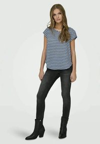 Top azul com padrão de diamantes e mangas curtas, combinado com jeans justos pretos e botas de tornozelo pretas. Tecido suave e ajuste tailored.