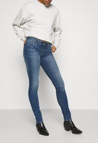 Jeans ajustados azules con una textura de denim suave, combinados con un sudadera holgada gris claro y botas de tacón negras.