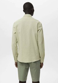 Hellgrünes, strukturiertes Langarmshirt mit einem Kragen, Knopfmanschetten und abgerundetem Saum. Kombiniert mit passenden grünen Shorts.