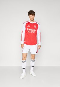 Arsenal FC fodboldtrøje med langt ærme i rød med hvide detaljer, hvide shorts og stribede sokker; lavet af glat stof.