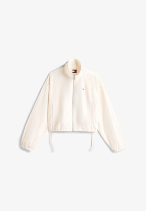 Veste légère blanche avec fermeture éclair frontale, poignets élastiques, ourlet à cordon de serrage, et petit logo rouge, blanc et bleu sur le côté gauche de la poitrine.