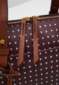 Sac à main violet avec motif de cœurs blancs, anses en cuir marron et fermetures éclair dorées.