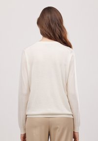 Kremowy, lekki sweter z długimi rękawami, okrągłym dekoltem i prążkowanymi mankietami. Gładka tekstura, minimalistyczny design, brak widocznych wzorów czy akcentów.