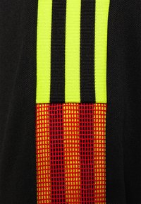 Tejido textil negro con tres rayas verticales amarillas y un patrón de cuadrícula roja texturizada. El diseño integra bloques de colores contrastantes.