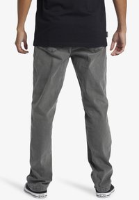 Gray denim jeans with a straight-leg design, featuring a textured finish and back pockets, paired with black shoes and a dark shirt.