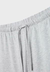 Szara, jasnoszara talia spodni dresowych z elastyczną gumką i zawiązanym sznurkiem na zbliżeniu tekstury tkaniny.