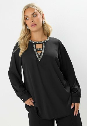 Camicia nera con maniche lunghe e scollo rotondo, caratterizzata da dettagli intricati in perline e ritagli sul davanti. Tessuto dalla texture liscia.