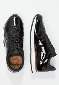 Baskets en cuir verni noir avec une languette texturée noire, des lacets ronds et des semelles en caoutchouc blanc, dotées d'une semelle intérieure en liège marquée "WODEN taille 37".