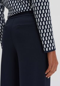 Pantaloni a gamba larga blu abbinati a un top in maglia con motivo a righe verticali e orizzontali in blu e bianco.