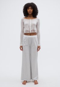 Φαρδιές πιτζάμες σε ανοιχτό γκρι χρώμα, συνδυασμένες με λευκό cropped μακρυμάνικο τοπ με δαντέλα και κουμπιά μπροστά.