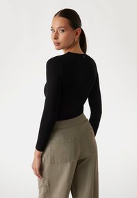 Maglione a maniche lunghe nero a coste con scollo rotondo, abbinato a pantaloni cargo verde oliva chiaro con molteplici tasche e cuciture minime.