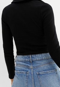 Schwarzes, geripptes Langarmoberteil mit runder Ausschnitt, kombiniert mit hellblauen, hoch taillierten Jeans. Die Jeans haben zwei Gesäßtaschen.