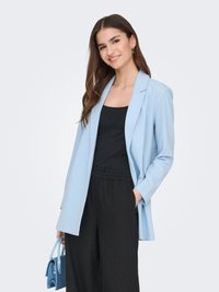 Light blue blazer made of soft fabric, featuring a relaxed fit with a single button, paired with a black top and loose black trousers.