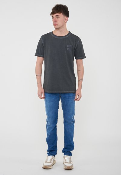 T-shirt di cotone grigio scuro con maniche corte e taschino. Indossato con jeans azzurri e sneaker beige, con lacci e dettagli bianchi.