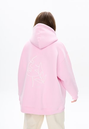 Oversized roze hoodie met een trekkoord in de capuchon, met een witte lijntekening van een gezicht en bladeren op de achterkant. Zachte textuur.