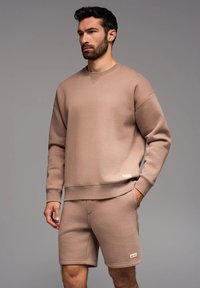 Beige Sweatshirt und passendes Shorts-Set, aus weichem Stoff gefertigt. Mit Rundhalsausschnitt, gerippten Bündchen und seitlichen Taschen an den Shorts.