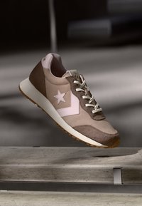 Sneaker beige e marrone realizzato in suede e tessuto, con un logo a stella rosa, lacci bianchi e una suola in gomma testurizzata.