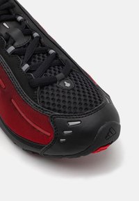 Sorte og røde sportsko med overdel i mesh, gummidetaljer, teksturert såle og refleksdetaljer. Buet tåhette-design.