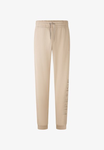 Beige Sweatpants aus weichem Stoff, mit einem elastischen Bund und Zugband, seitlichen Taschen und einem bedruckten Logo entlang eines Beins.