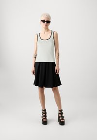 Lys grøn tanktop med sort trim, parret med en sort flared nederdel. Båret med klodsede sorte platform sandaler. Glat tekstur hele vejen igennem.