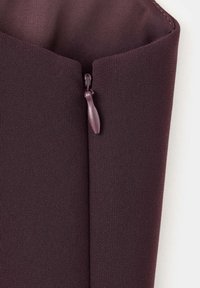 Gros plan d'une fermeture éclair en tissu violet foncé avec une languette en tissu assortie sur un fond clair.