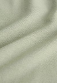 Glad lichtgroen stof met zichtbare fijne breistructuur en zachte plooien die zachte schaduwen creëren.