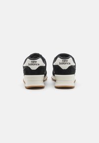 Black suede and mesh athletic shoes with white accents and "new balance" logo on heel, featuring a light rubber sole with a textured finish.