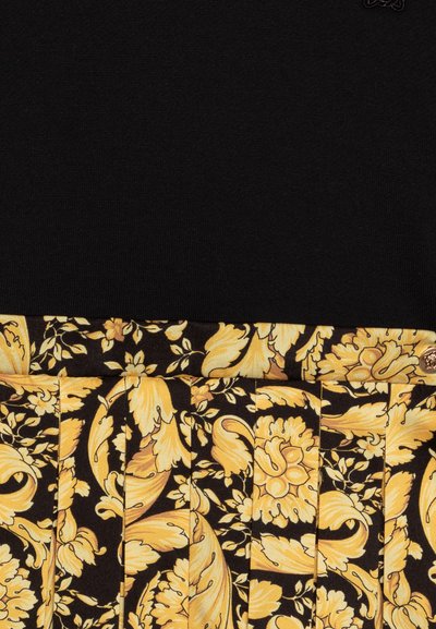 Top de punto negro con una vibrante falda floral plisada. La falda presenta flores amarillas y hojas sobre un fondo negro, añadiendo textura y contraste.